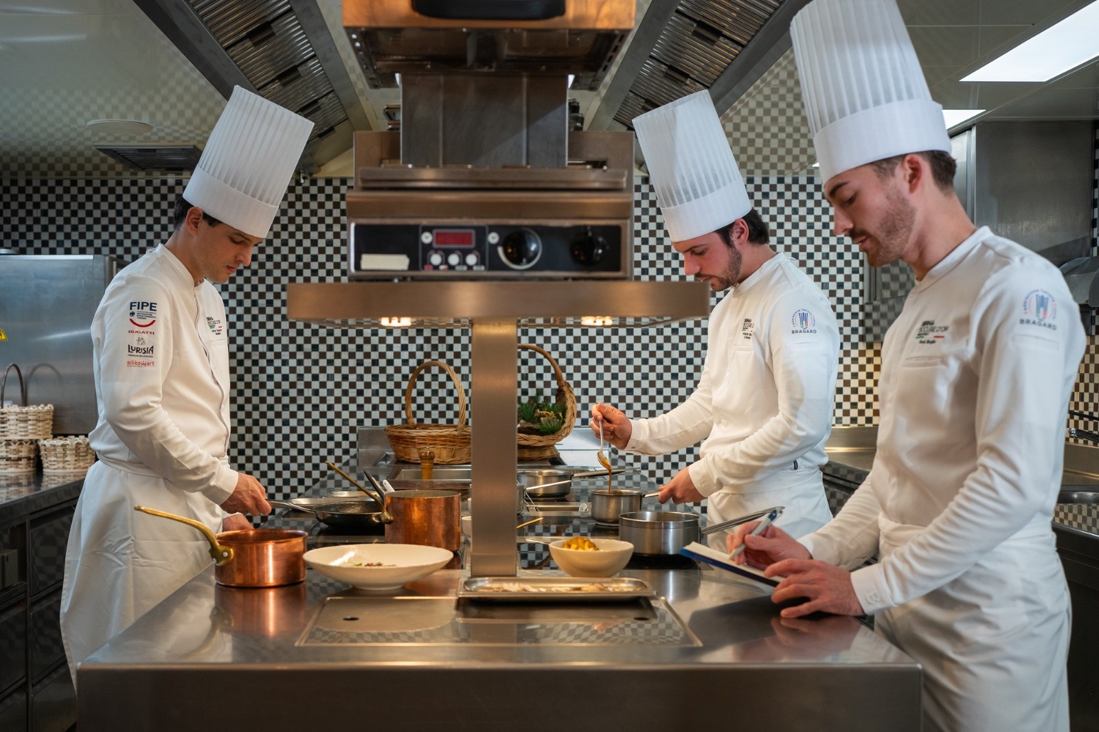 Tre giovani cuochi in toque al lavoro in una cucina professionale