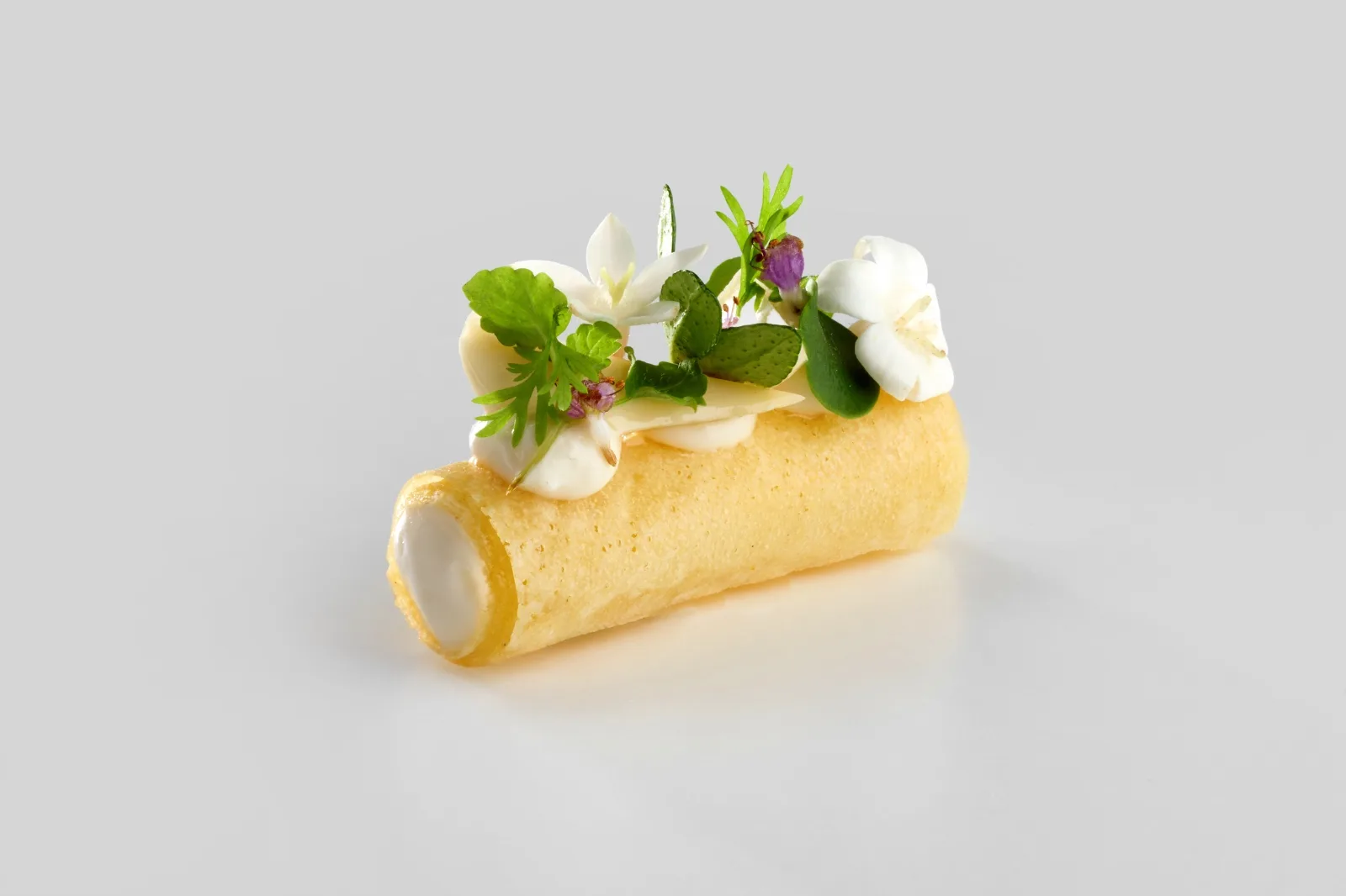 Cannolo croccante farcito di crema, con erbe fresche e fiori bianchi